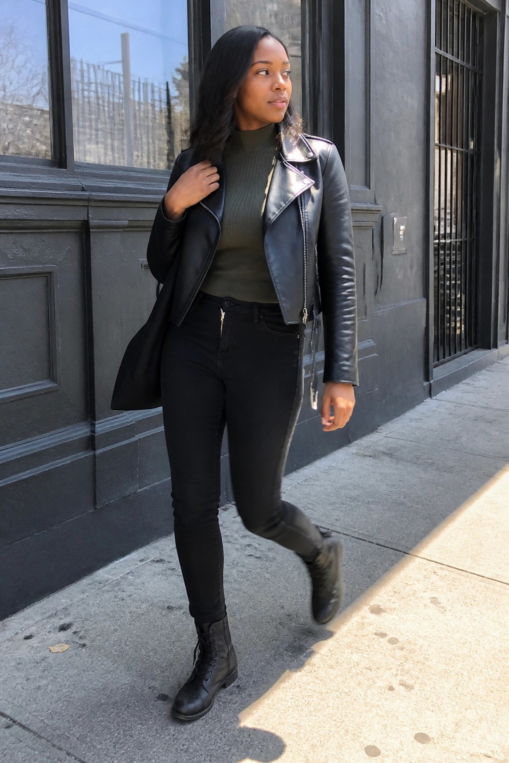 Woman in black leather jacket and green turtleneck on urban sidewalk