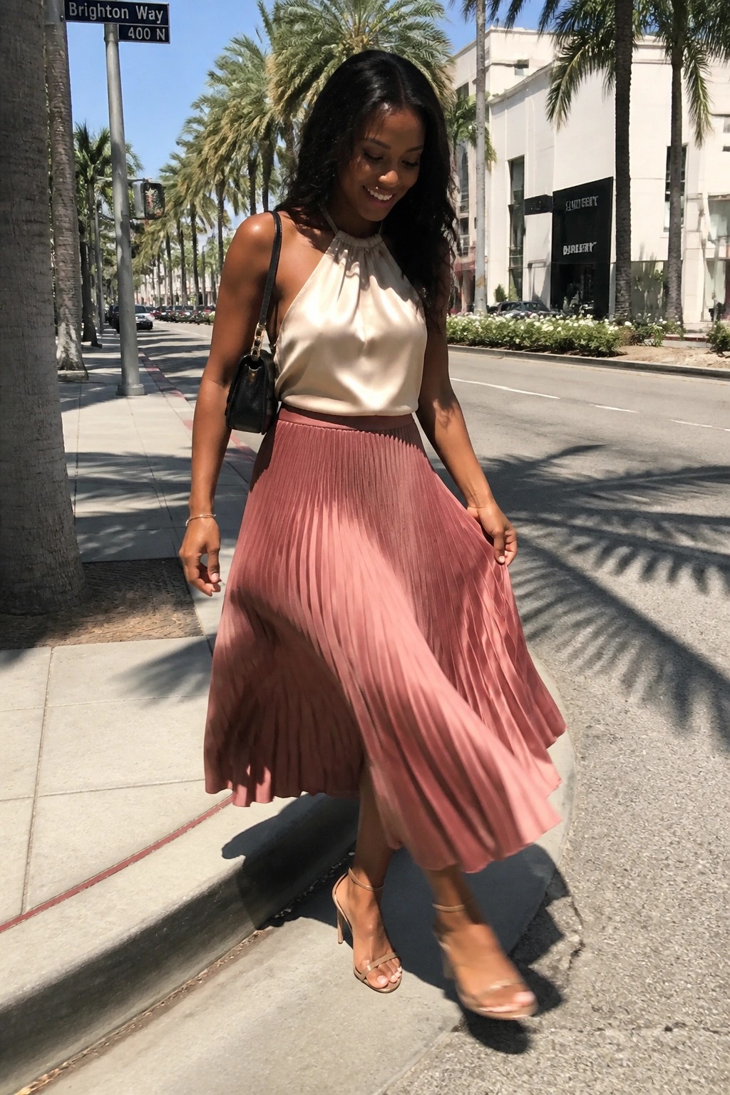 Woman in beige halter top and pink pleated skirt on sunny palm-lined street