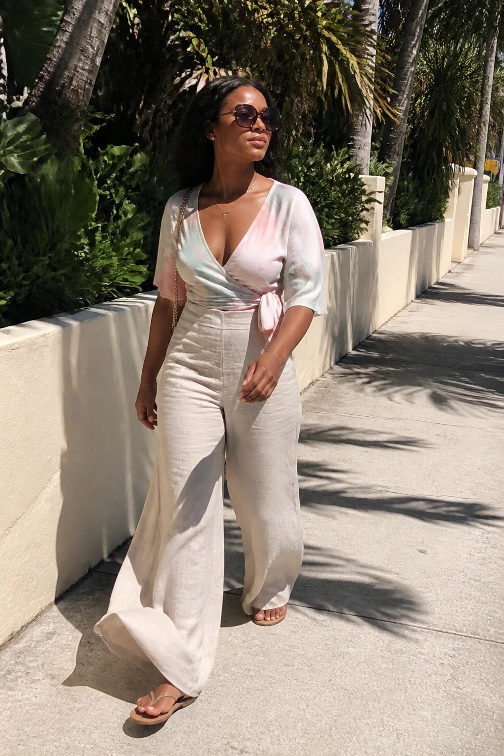 Woman in pastel tie-dye wrap top and white wide-leg pants on sunny sidewalk