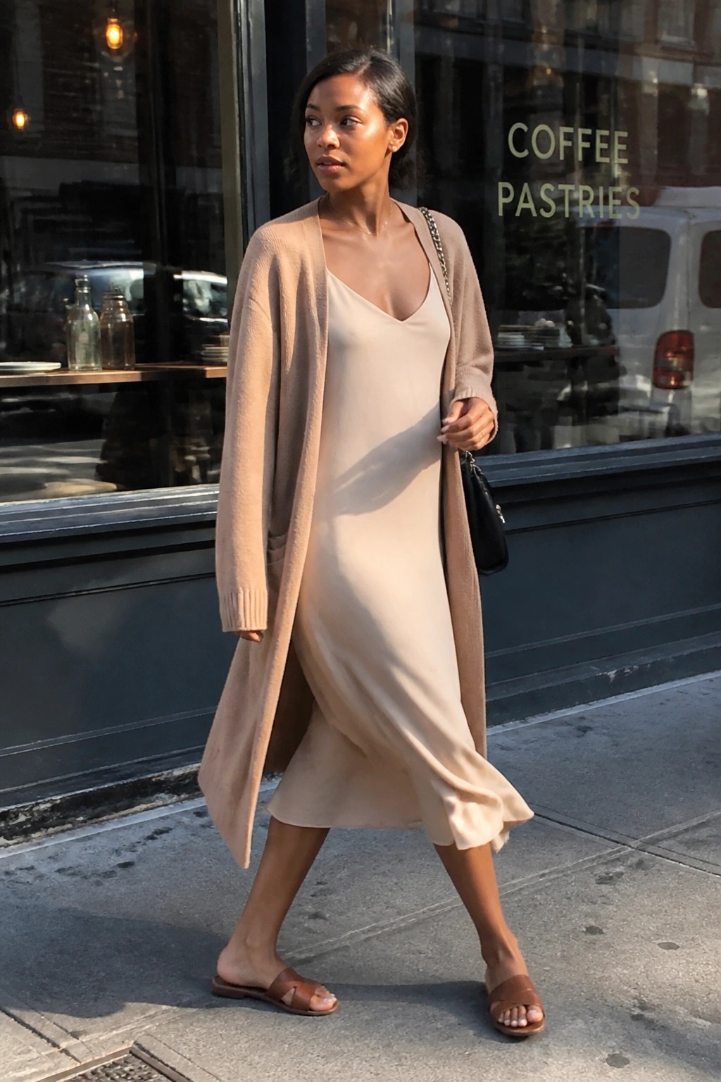 Woman in beige cardigan over satin slip dress outside coffee shop window