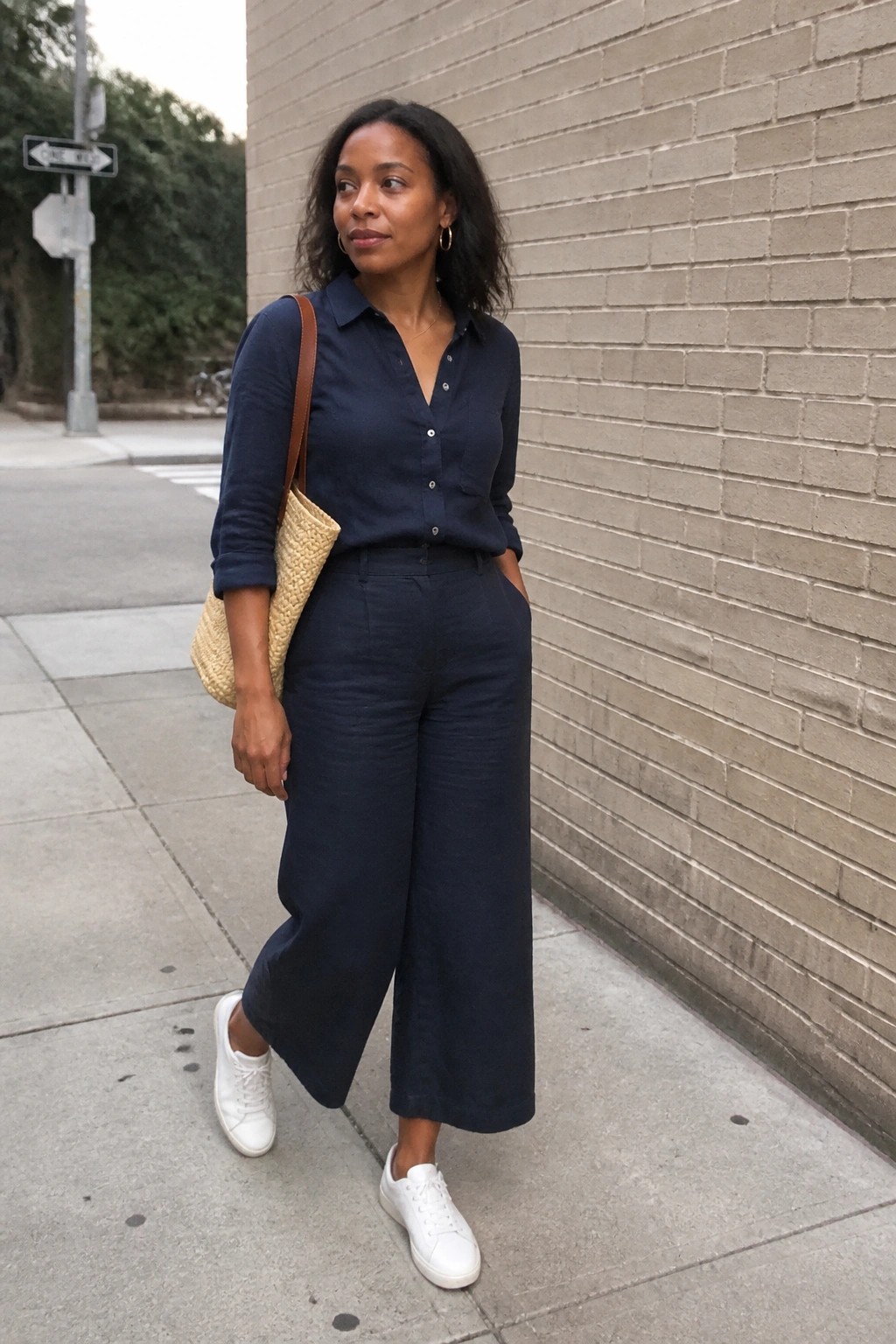 Woman in navy blue linen shirt and wide pants with white sneakers and woven bag