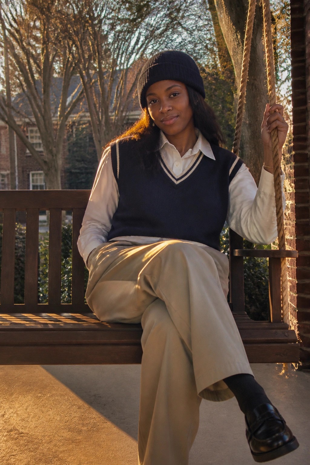 Young Black woman in beanie and navy vest on wooden porch swing