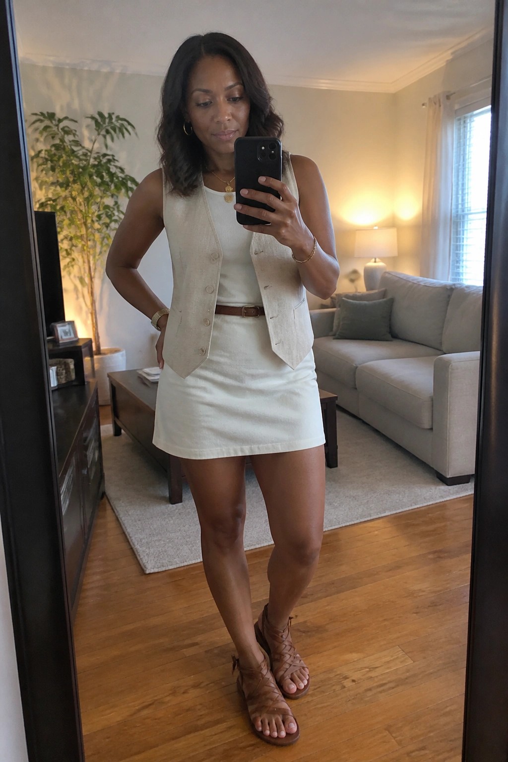 Woman in cream linen vest and skirt taking mirror selfie in living room