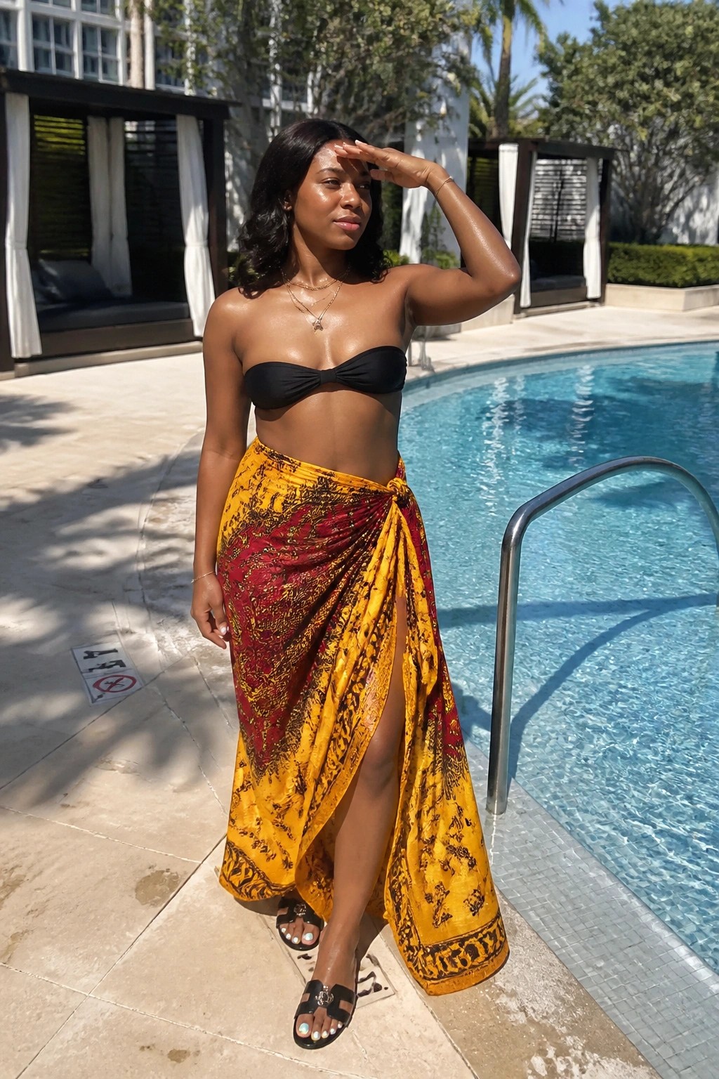 Woman in black strapless top and yellow-red patterned sarong posing by pool