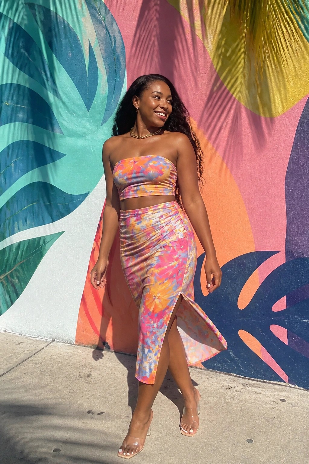 Woman in colorful floral two-piece outfit posing before vibrant mural wall.