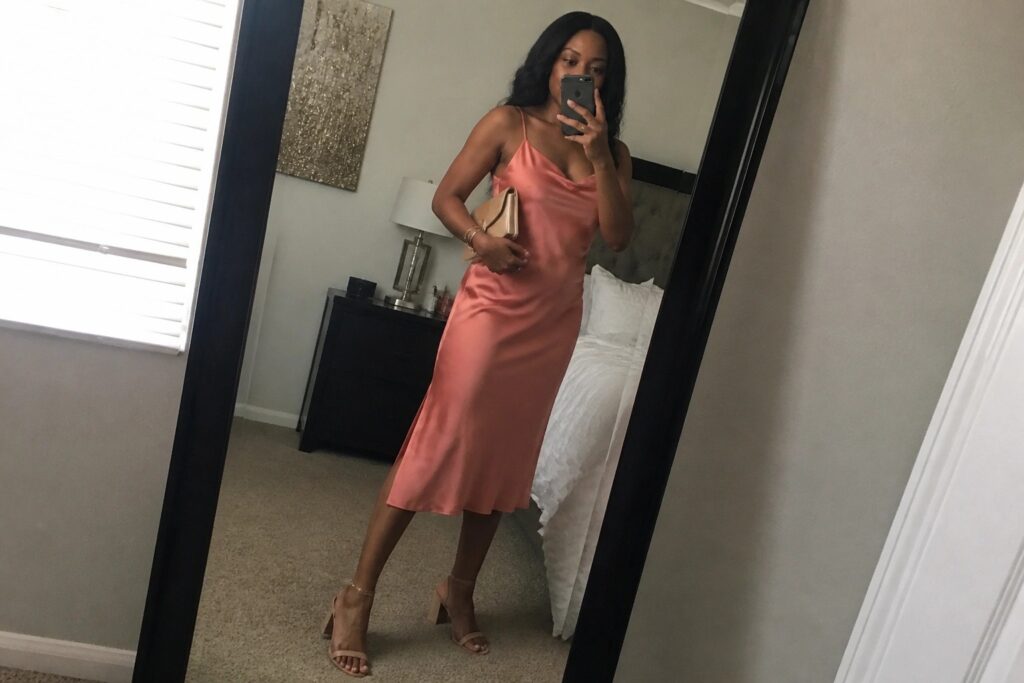 Woman in long peach satin dress taking mirror selfie in bedroom with strappy heels