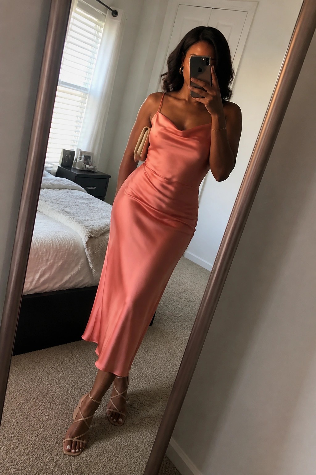 Woman in long peach satin dress taking mirror selfie in bedroom with strappy heels