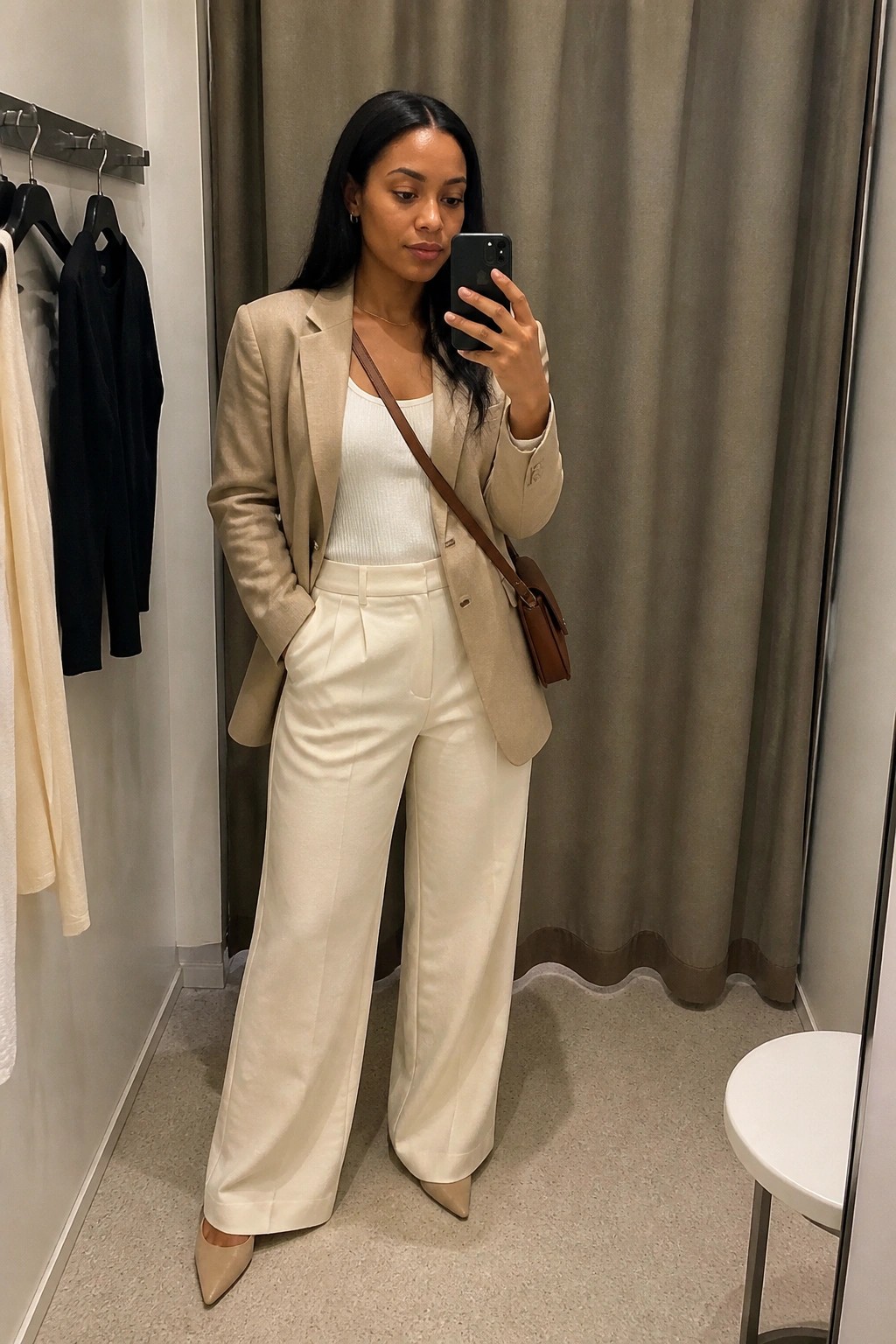 Woman in beige blazer and white wide-leg pants taking mirror selfie in fitting room