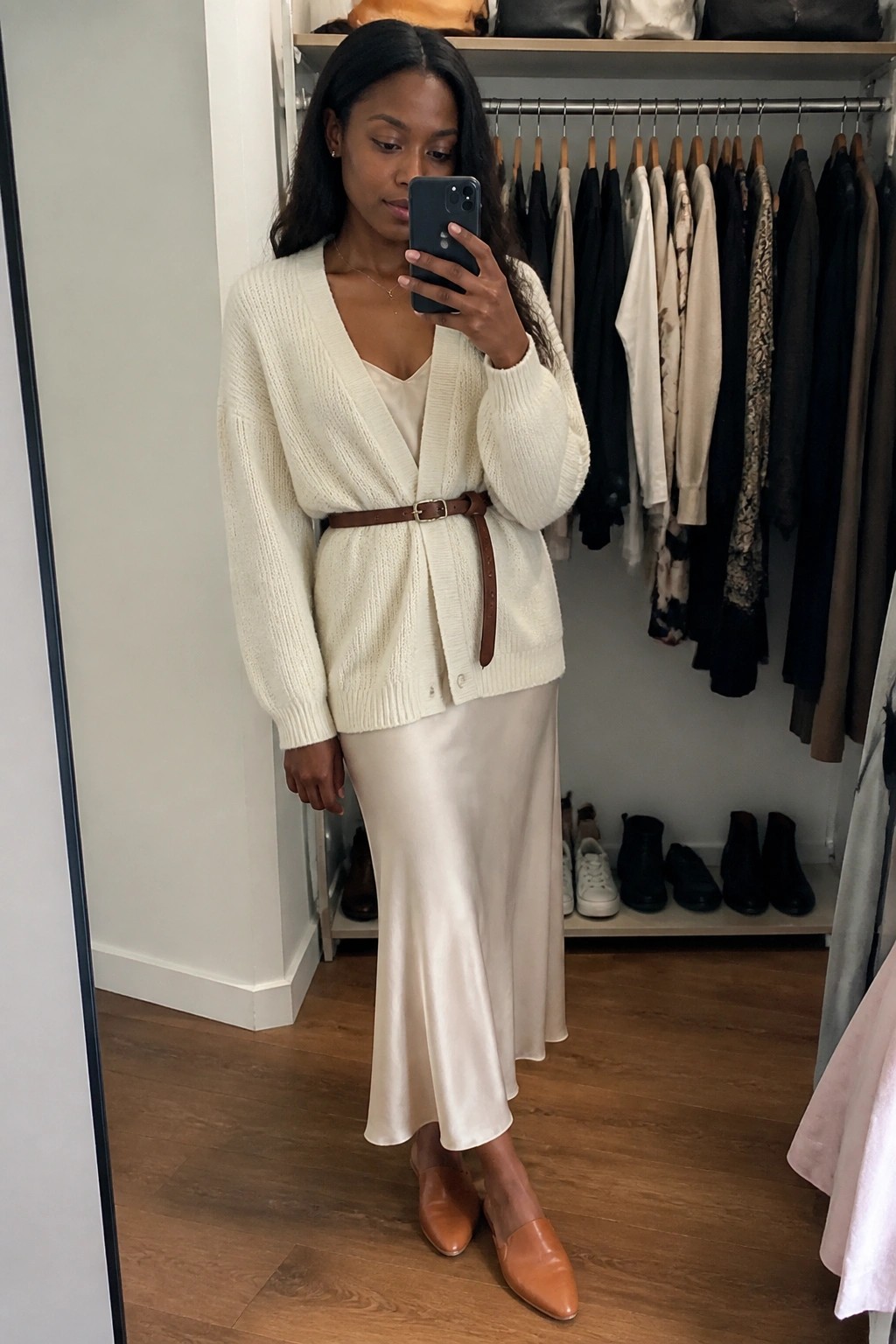 Woman in cream cardigan and beige satin dress taking closet mirror selfie