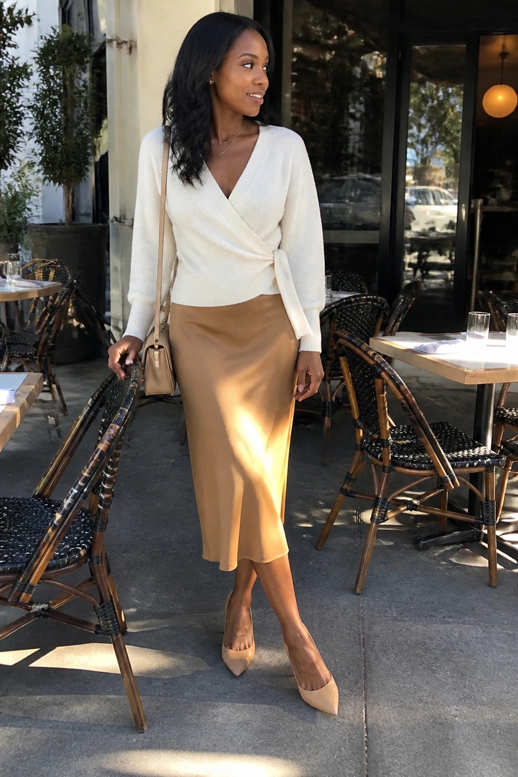 Woman in white wrap sweater and tan midi skirt at outdoor cafe