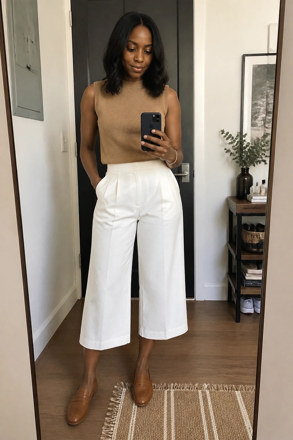 Woman in tan sleeveless top and white wide-leg pants taking mirror selfie