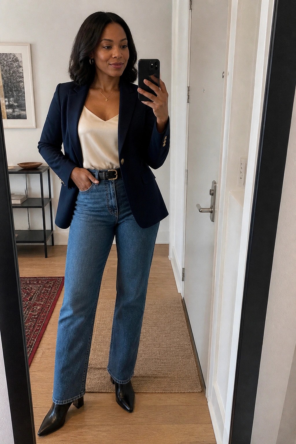 Woman in navy blazer and jeans taking mirror selfie with phone