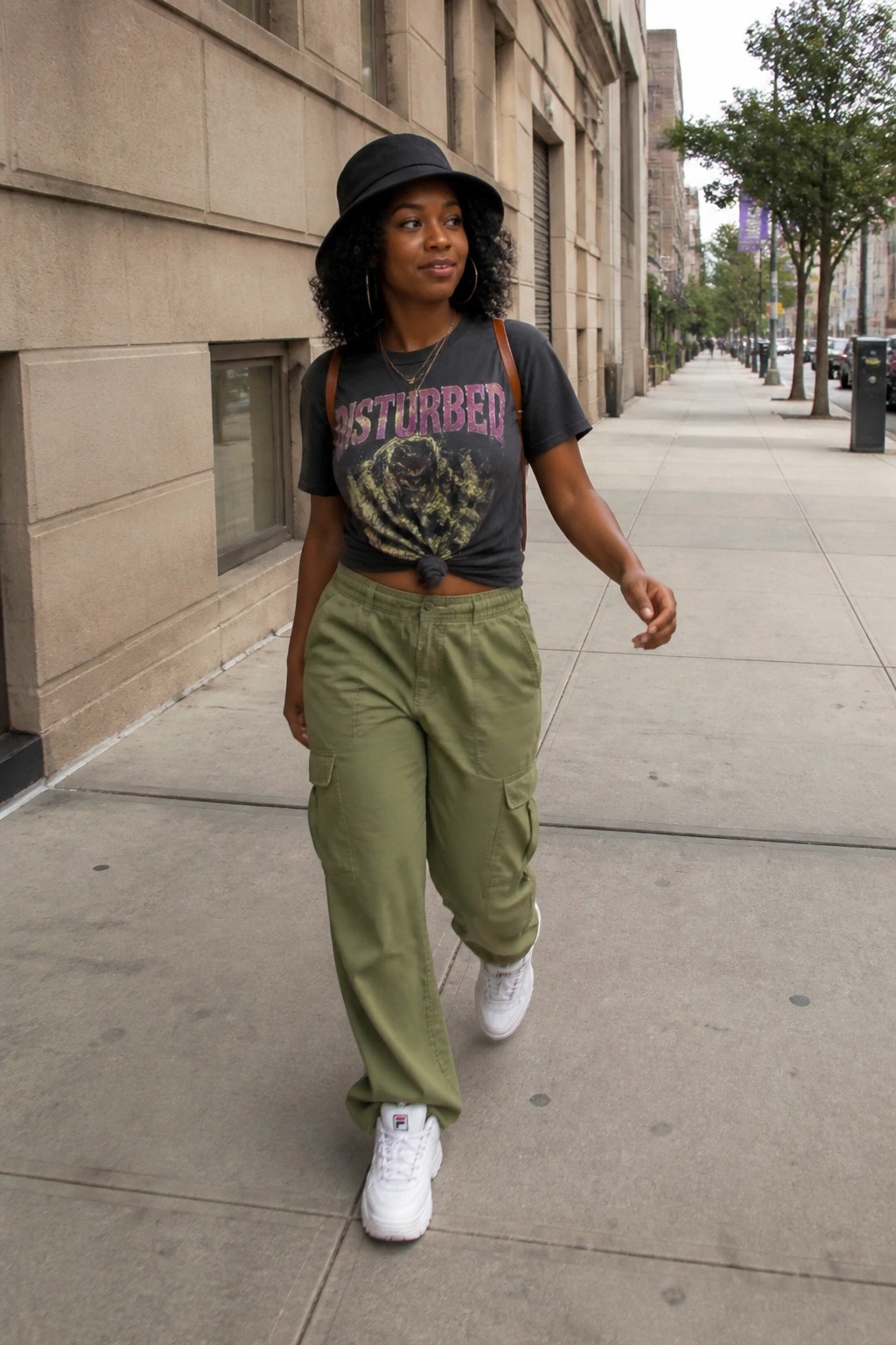 Woman in black hat, Disturbed tee, and olive cargo pants on city sidewalk