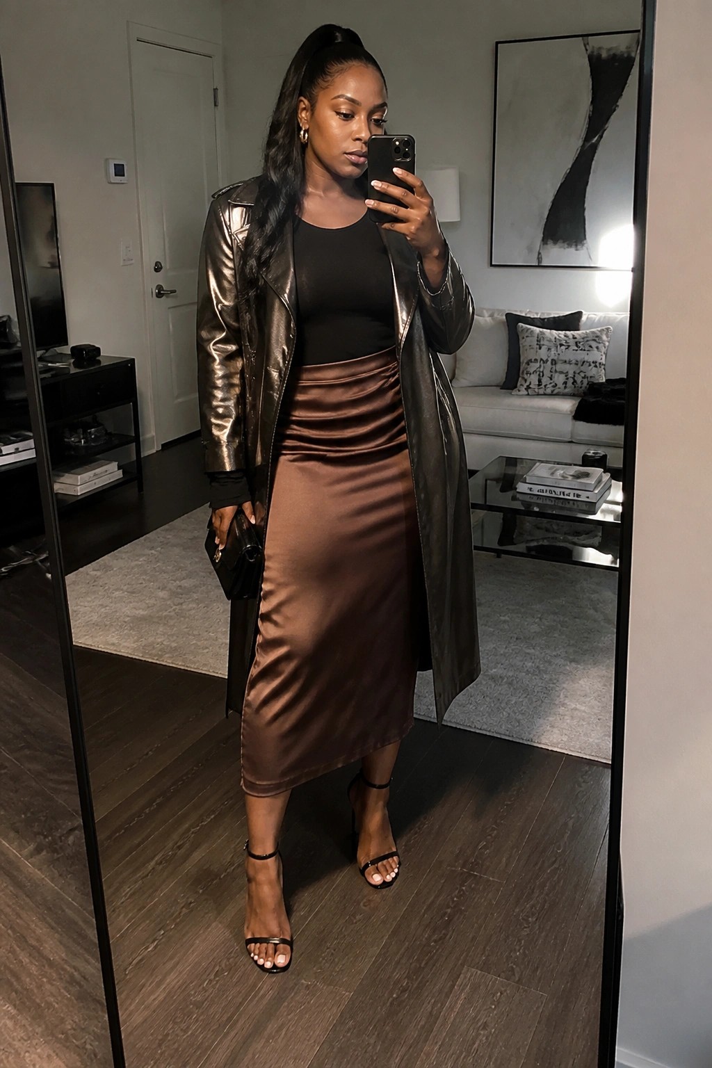Woman in brown satin skirt and metallic jacket taking mirror selfie in living room