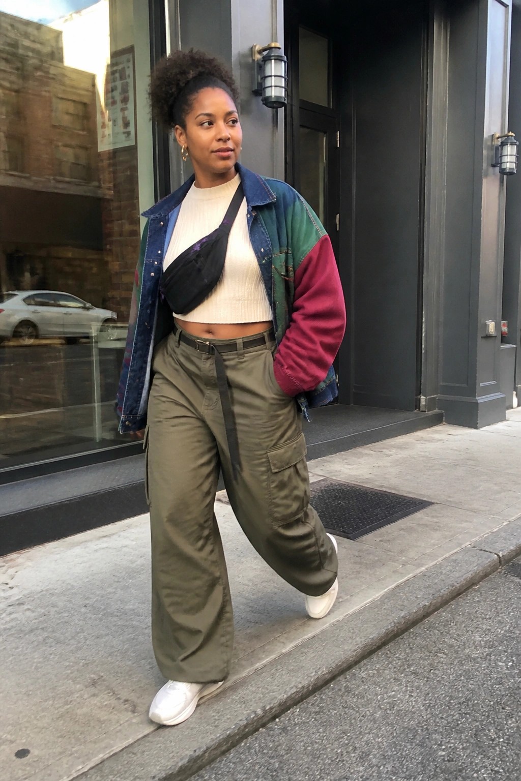 Woman in patchwork denim jacket, olive cargo pants, and white sneakers on sidewalk