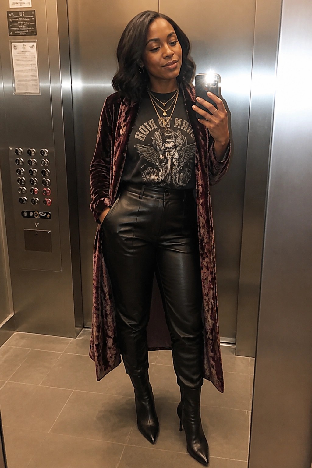 Woman in maroon velvet coat and black leather pants selfies in elevator
