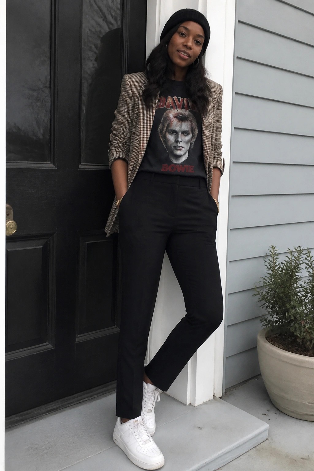Woman in houndstooth blazer over Bowie t-shirt, black pants, white sneakers by black door.
