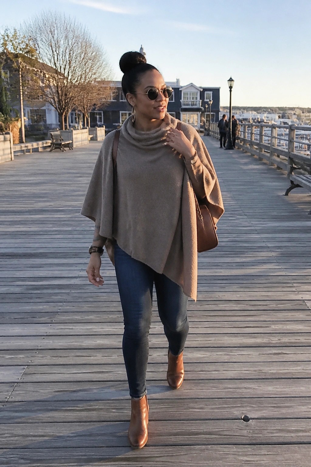 Woman in beige poncho sweater and jeans walking on sunny wooden pier