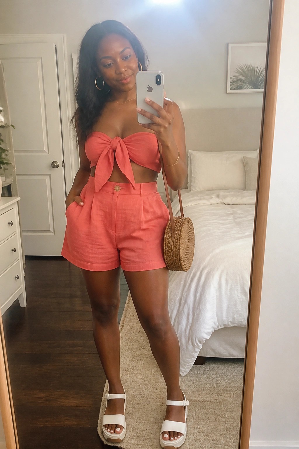 Woman in coral pink bow-front top and matching shorts taking bedroom mirror selfie