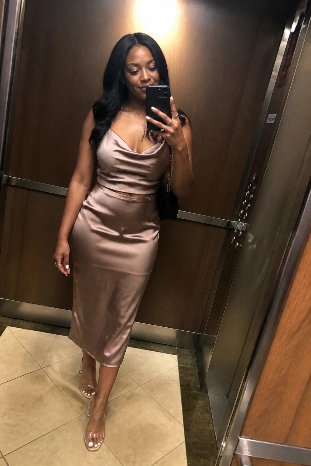 Woman in beige satin crop top and midi skirt taking elevator selfie