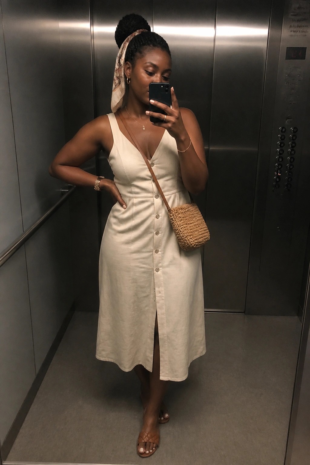 Woman in cream button-front dress taking selfie in elevator with woven bag