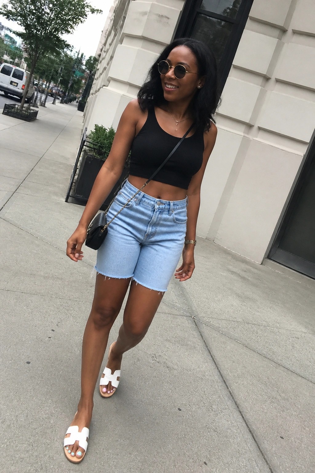 Woman in black crop top and light blue denim shorts on city sidewalk