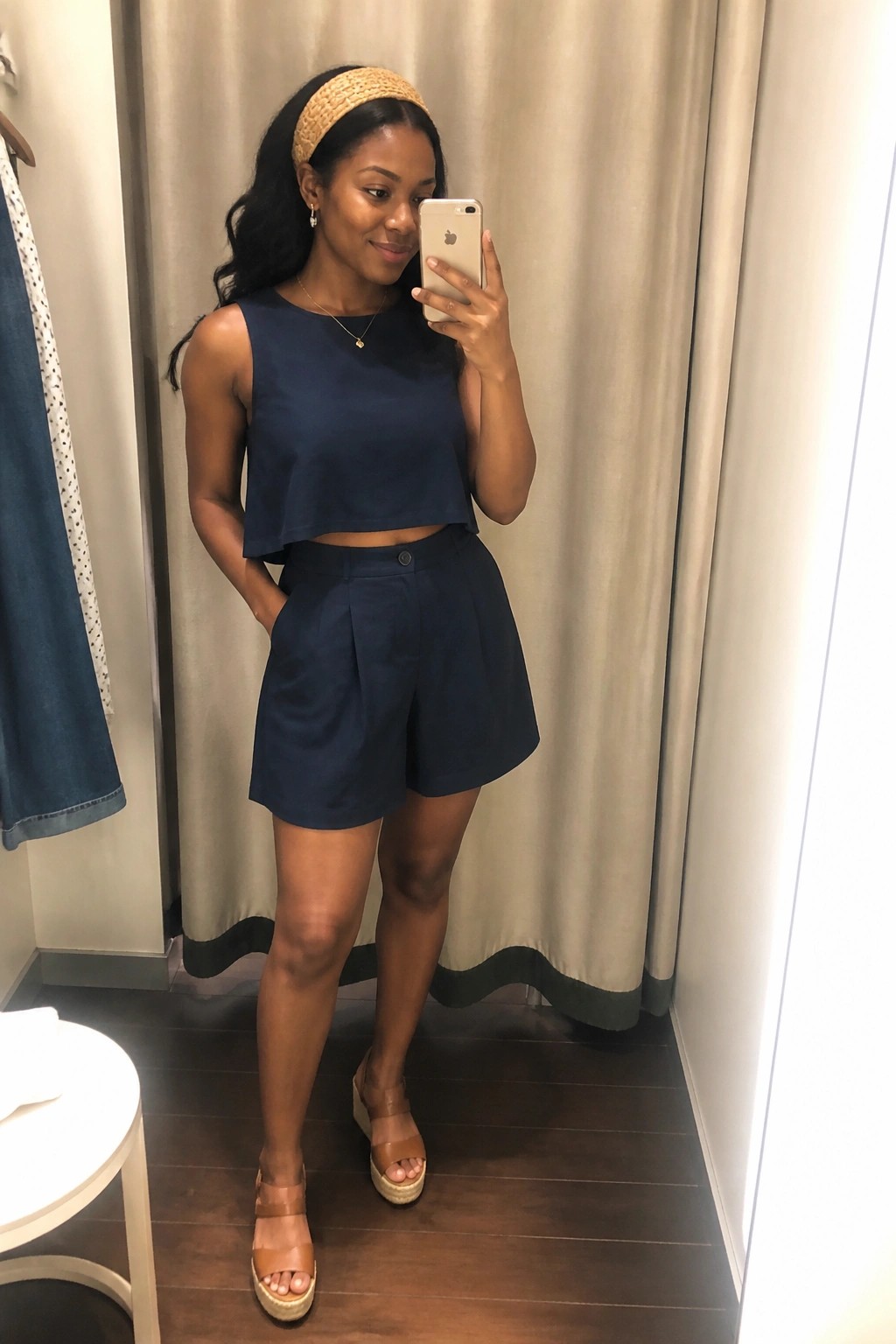 Woman in navy blue crop top and shorts taking mirror selfie in fitting room