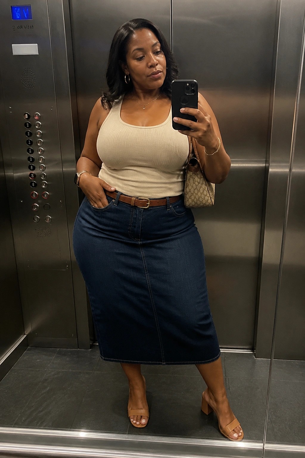 Woman in beige tank top and denim skirt taking selfie in elevator