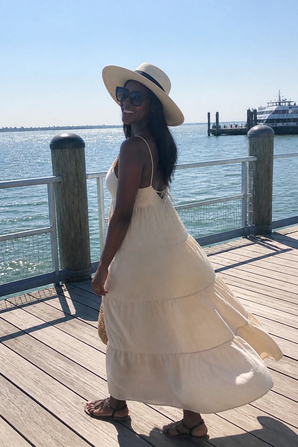 Woman in cream tiered sundress and straw hat on sunny wooden waterfront dock