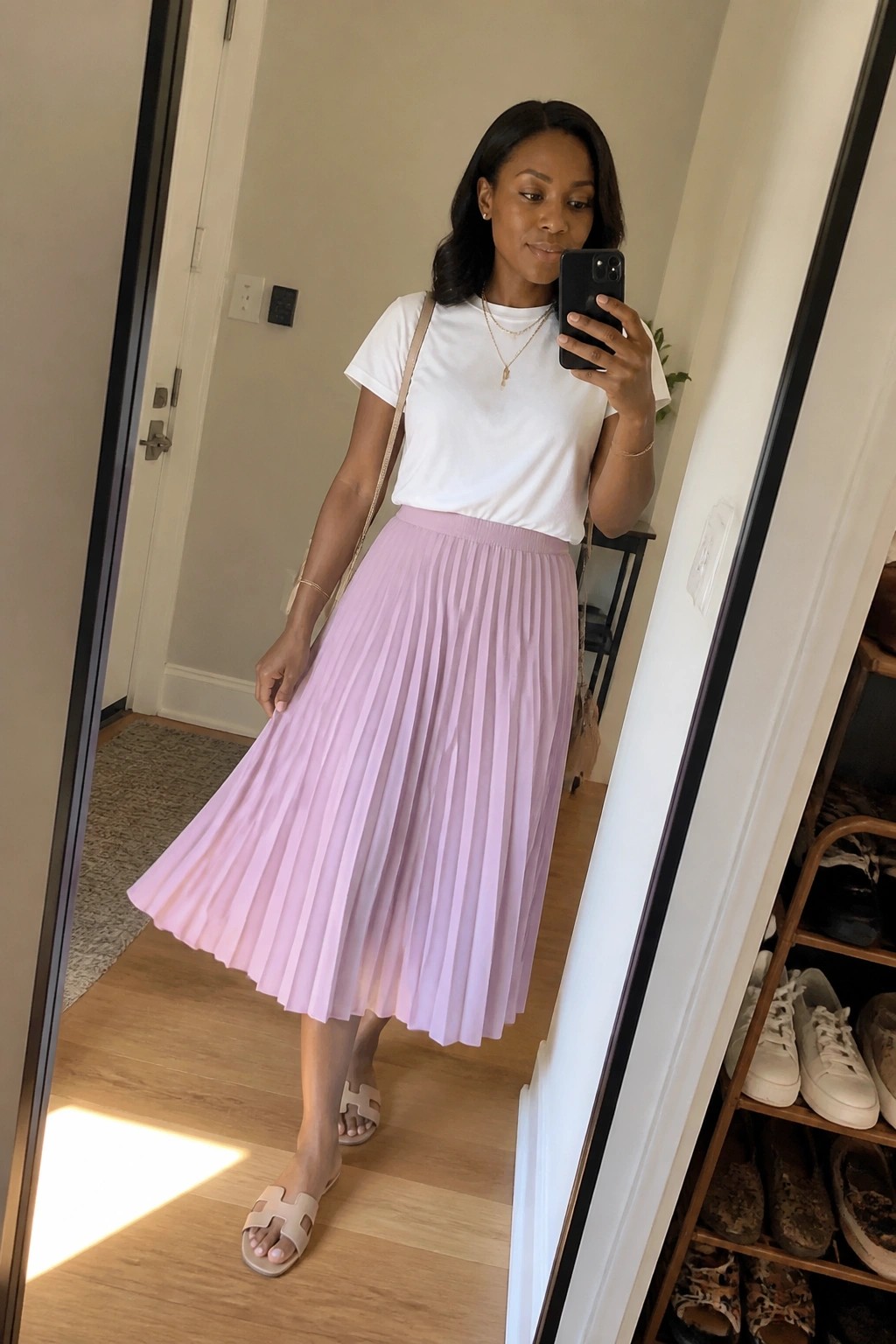 Woman in white t-shirt and lavender pleated skirt takes mirror selfie with phone