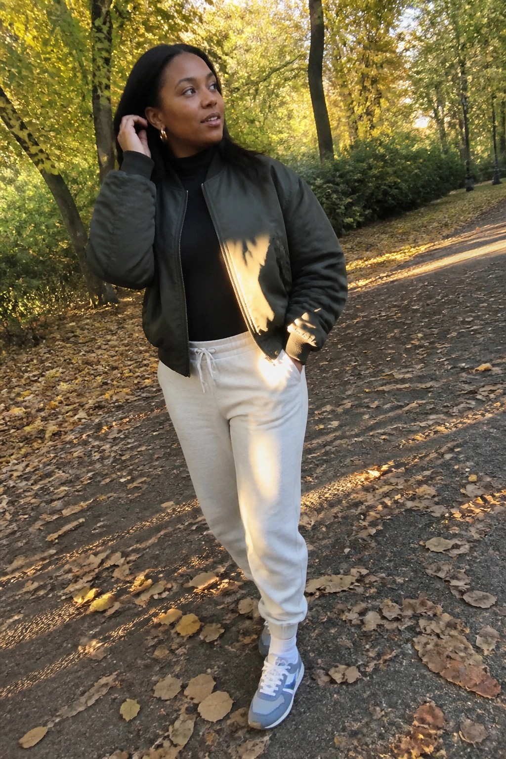 Woman in green bomber jacket and beige sweatpants on autumn path in park