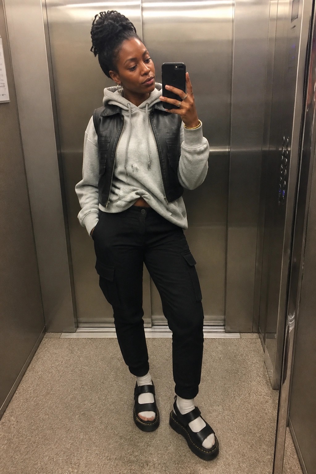 Woman in grey hoodie and black leather vest taking elevator selfie