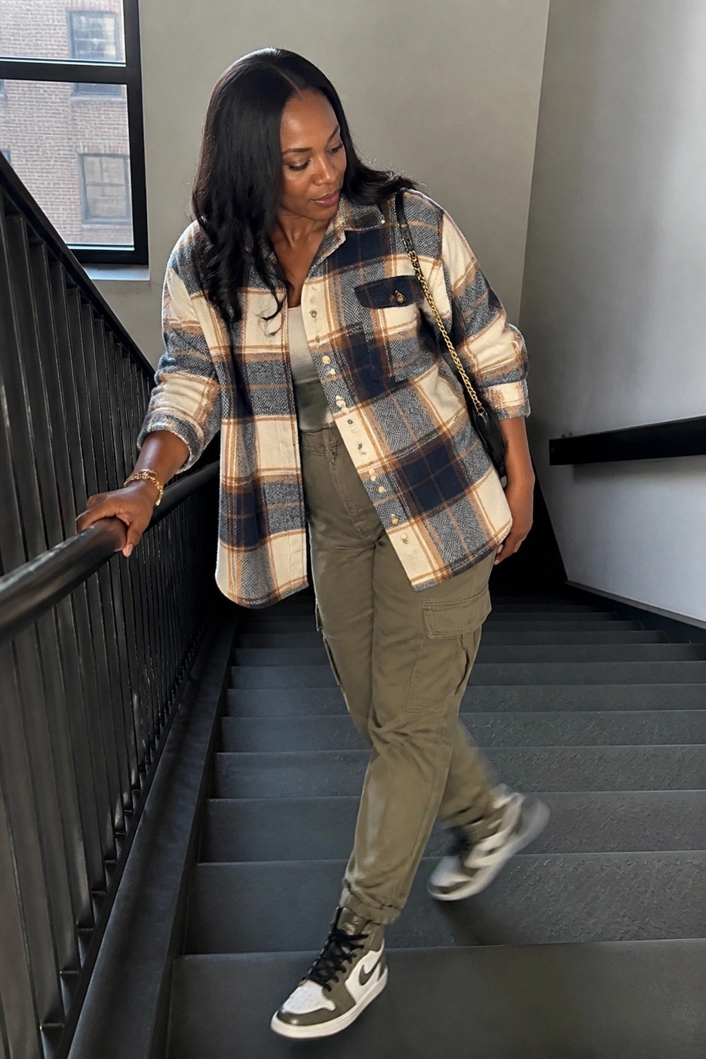 Woman in plaid shirt and cargo pants descending gray stairs holding railing