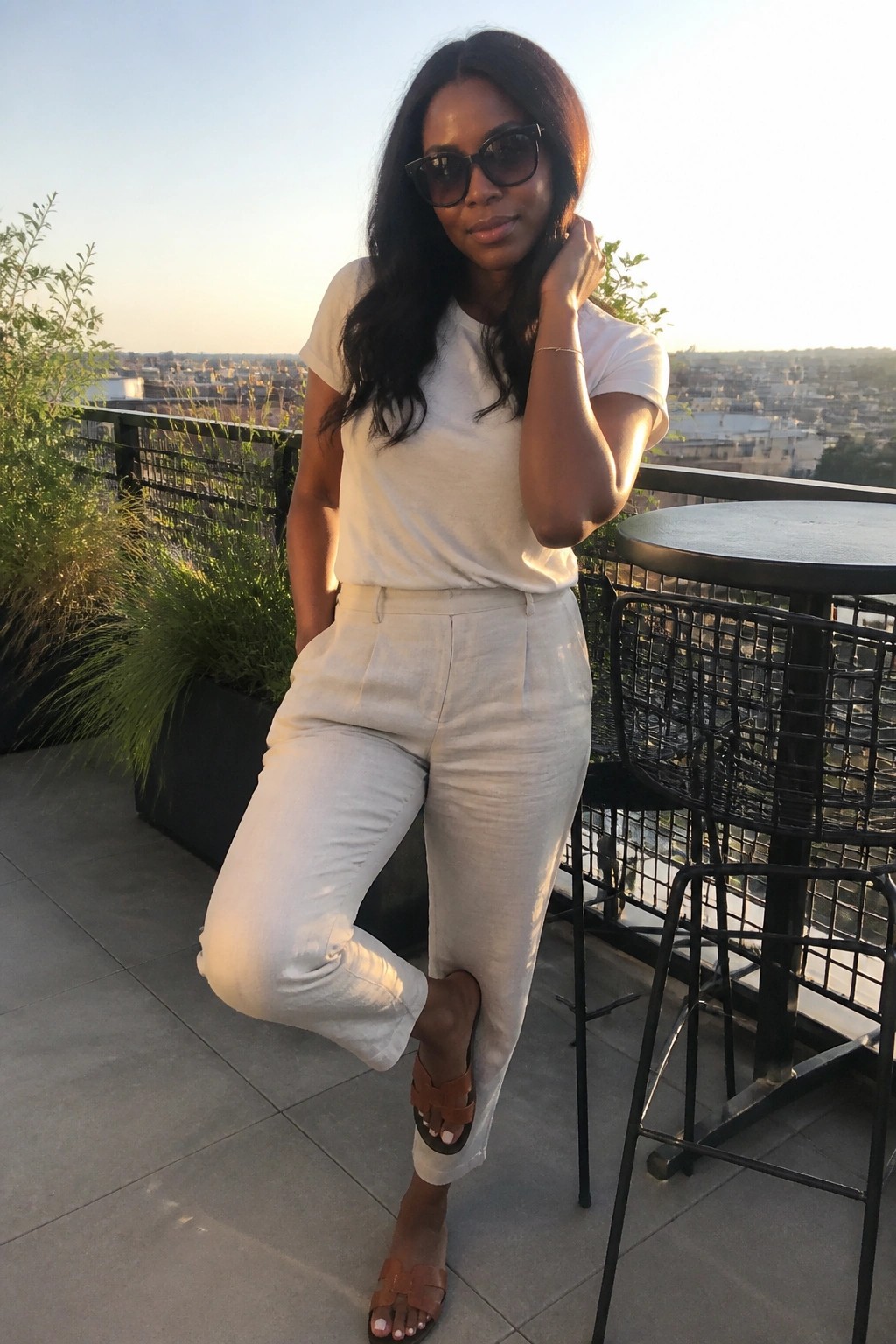 Woman in white outfit and sunglasses posing on sunset city rooftop terrace