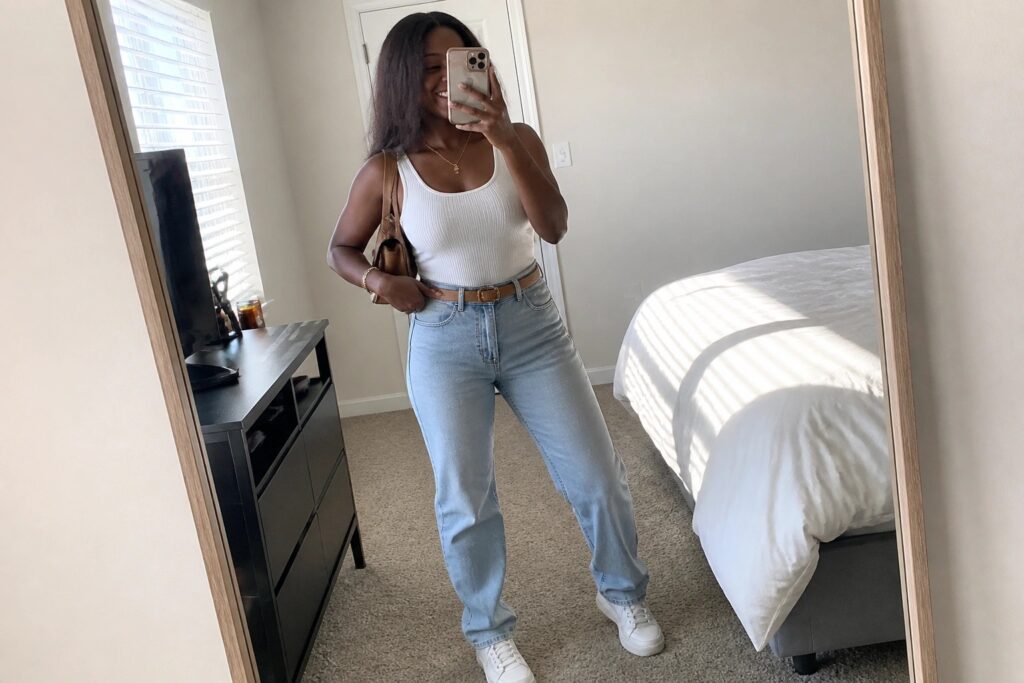 24 Casual Outfits for Black Women That Feel Comfortable and Put Together Woman in white ribbed crop top and light-wash jeans taking mirror selfie in bedroom
