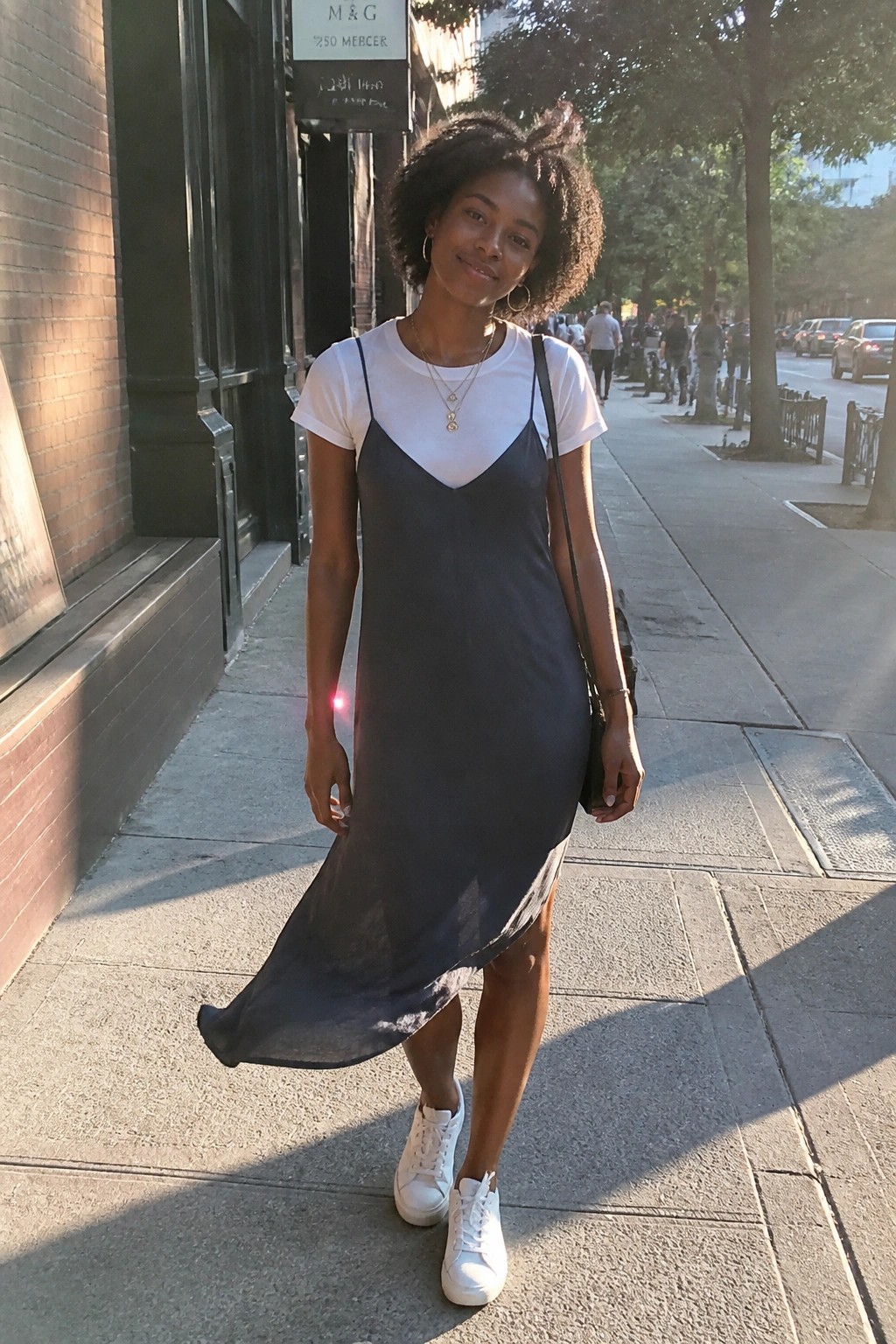 Woman in gray slip dress over white tee on sunny city sidewalk