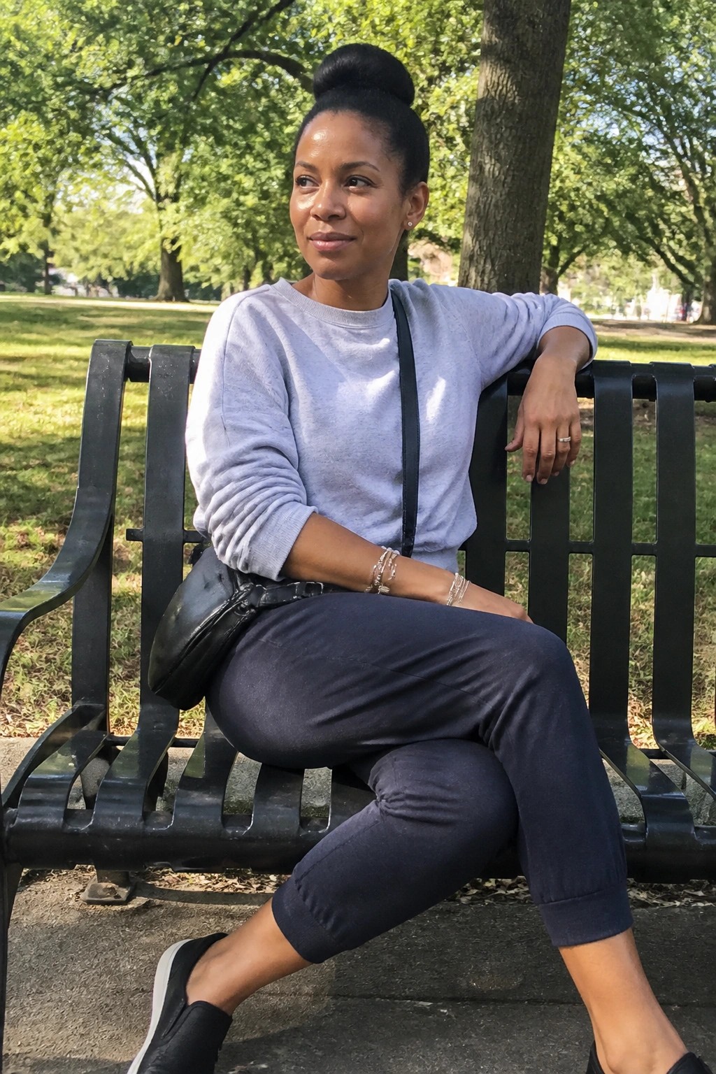 Woman in gray sweatshirt and navy pants seated on black park bench