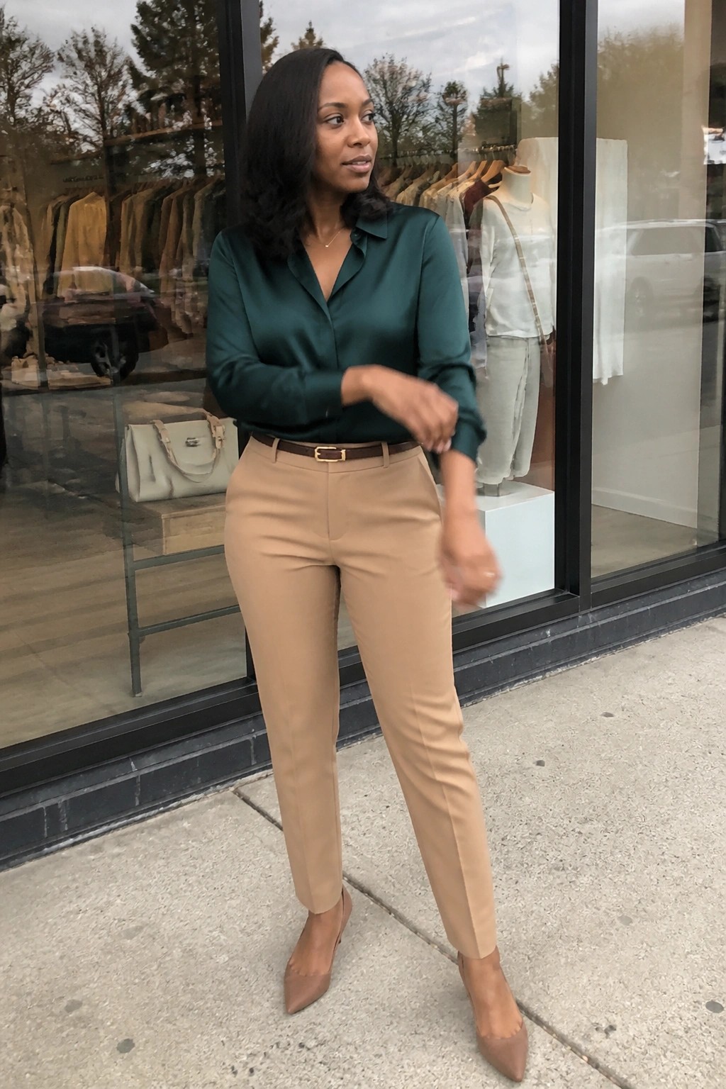 Woman in green satin blouse and tan pants outside clothing store window