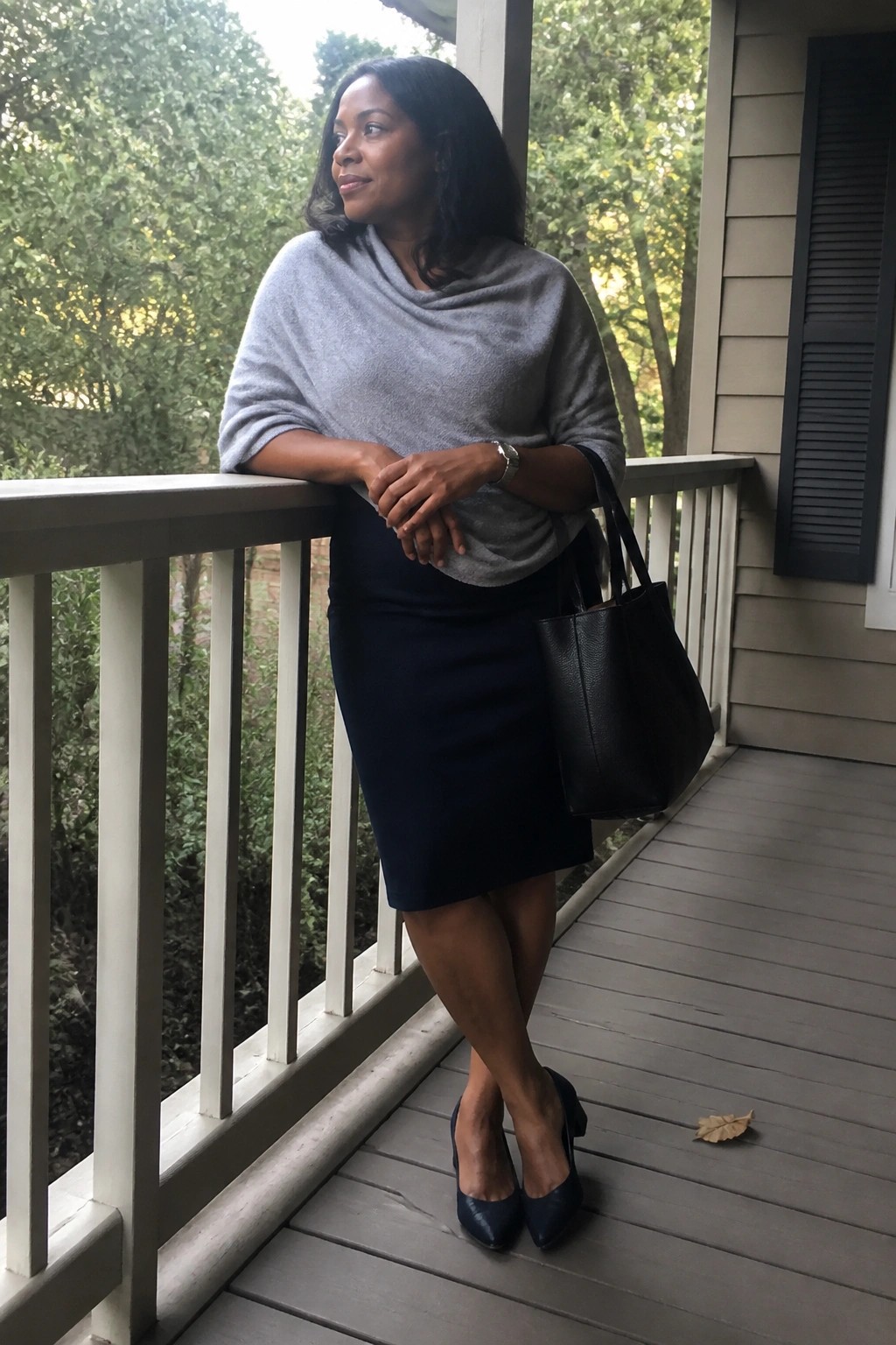 Woman in gray sweater and navy skirt on porch with black tote bag