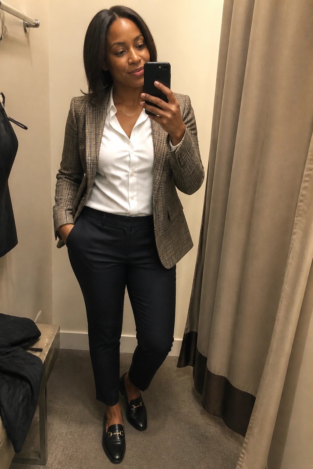 Woman taking a mirror selfie in a plaid blazer over a white button-up shirt paired with black pants and black loafers with gold hardware.