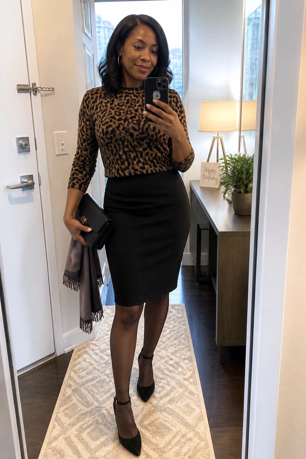 Woman in leopard-print top and black skirt taking mirror selfie with phone