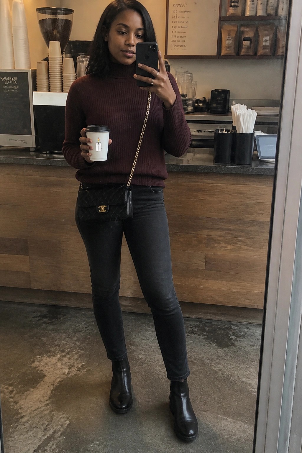 Woman in maroon turtleneck taking mirror selfie with coffee cup in cafe