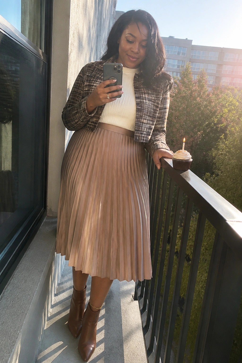 Woman in plaid jacket and pleated skirt with phone and lit cupcake on balcony
