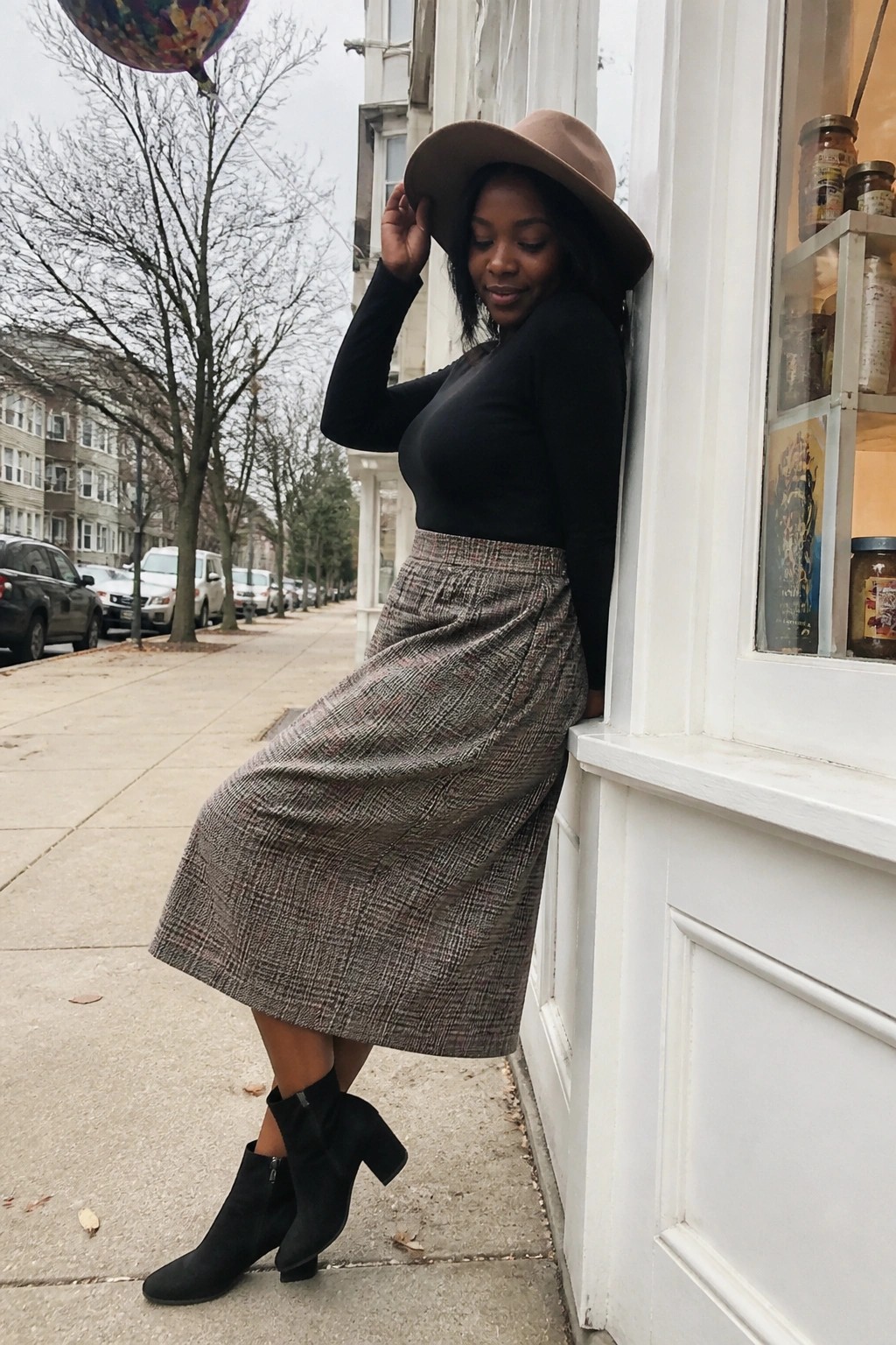 Woman in black top and plaid skirt with brown hat on city sidewalk