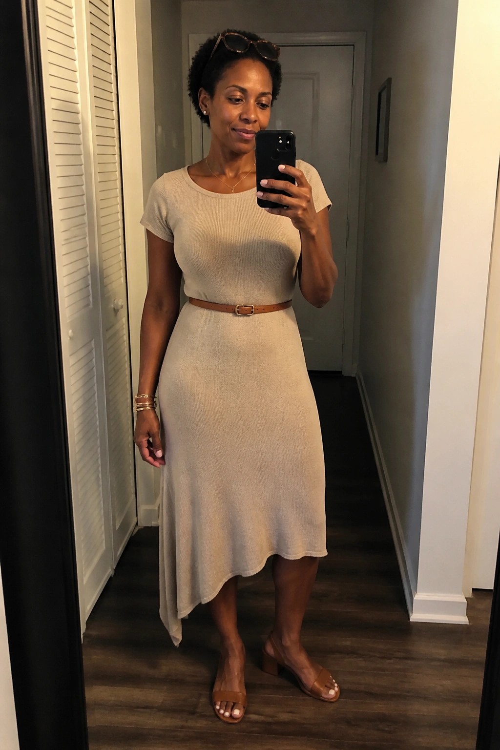 Woman in beige knit midi dress with brown belt taking mirror selfie in hallway