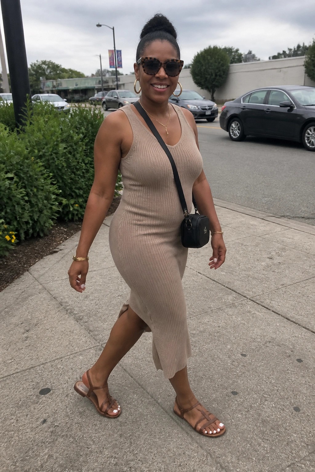 Woman in beige ribbed dress with black bag walking on sidewalk wearing sunglasses