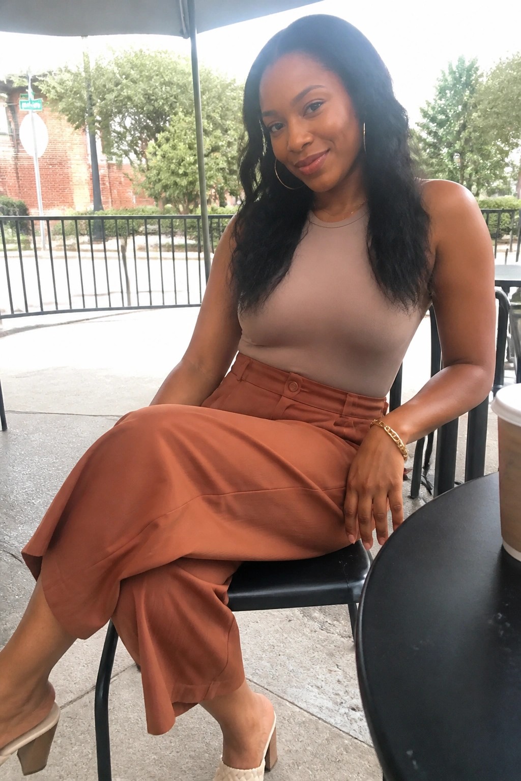 Woman in beige top and rust pants seated at outdoor table with coffee