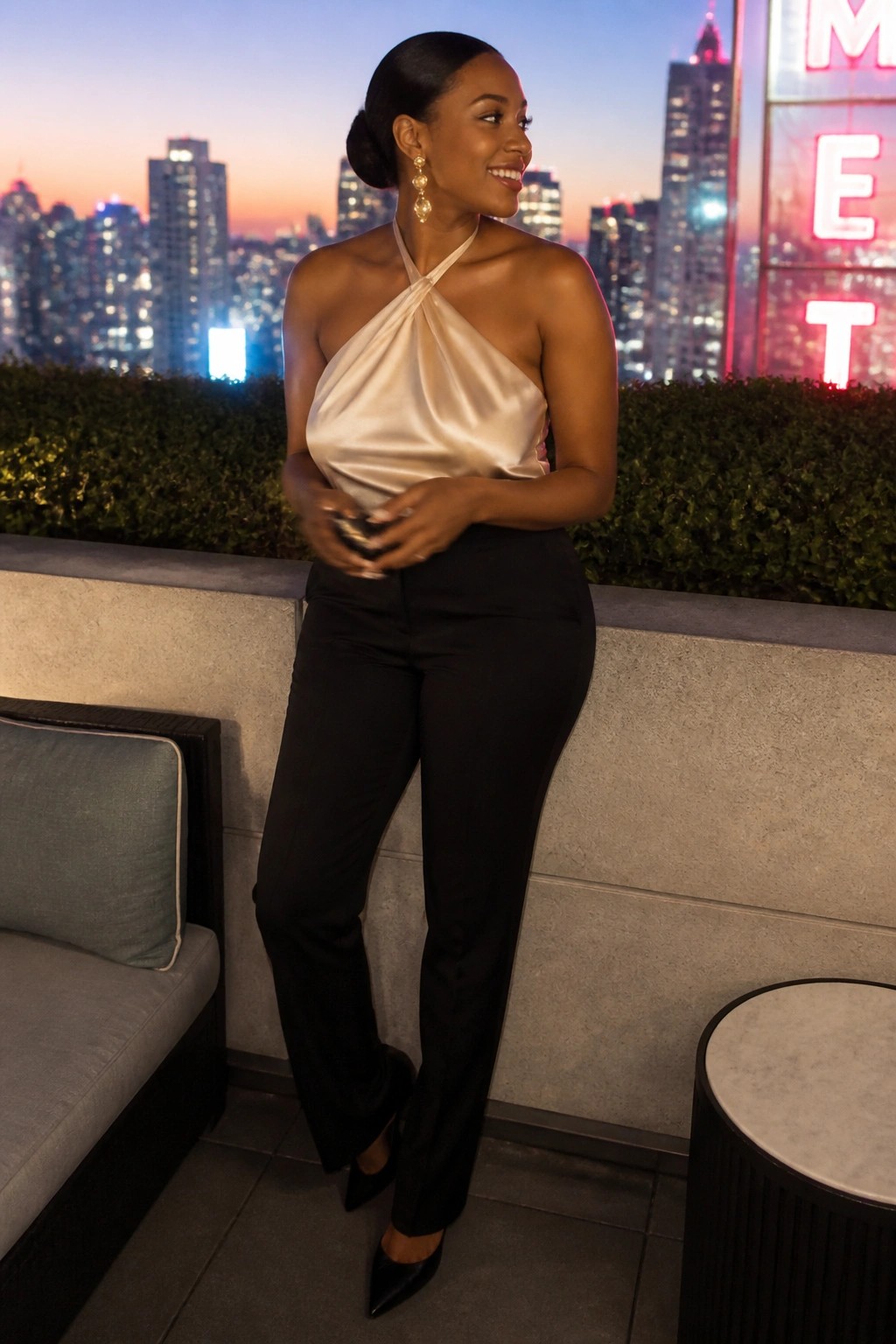 Woman in champagne satin halter top and black pants on city rooftop at dusk