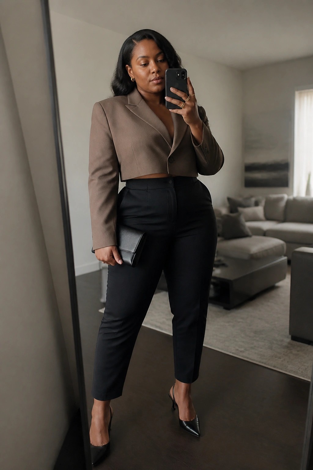 Woman in cropped taupe blazer and black pants taking mirror selfie with phone