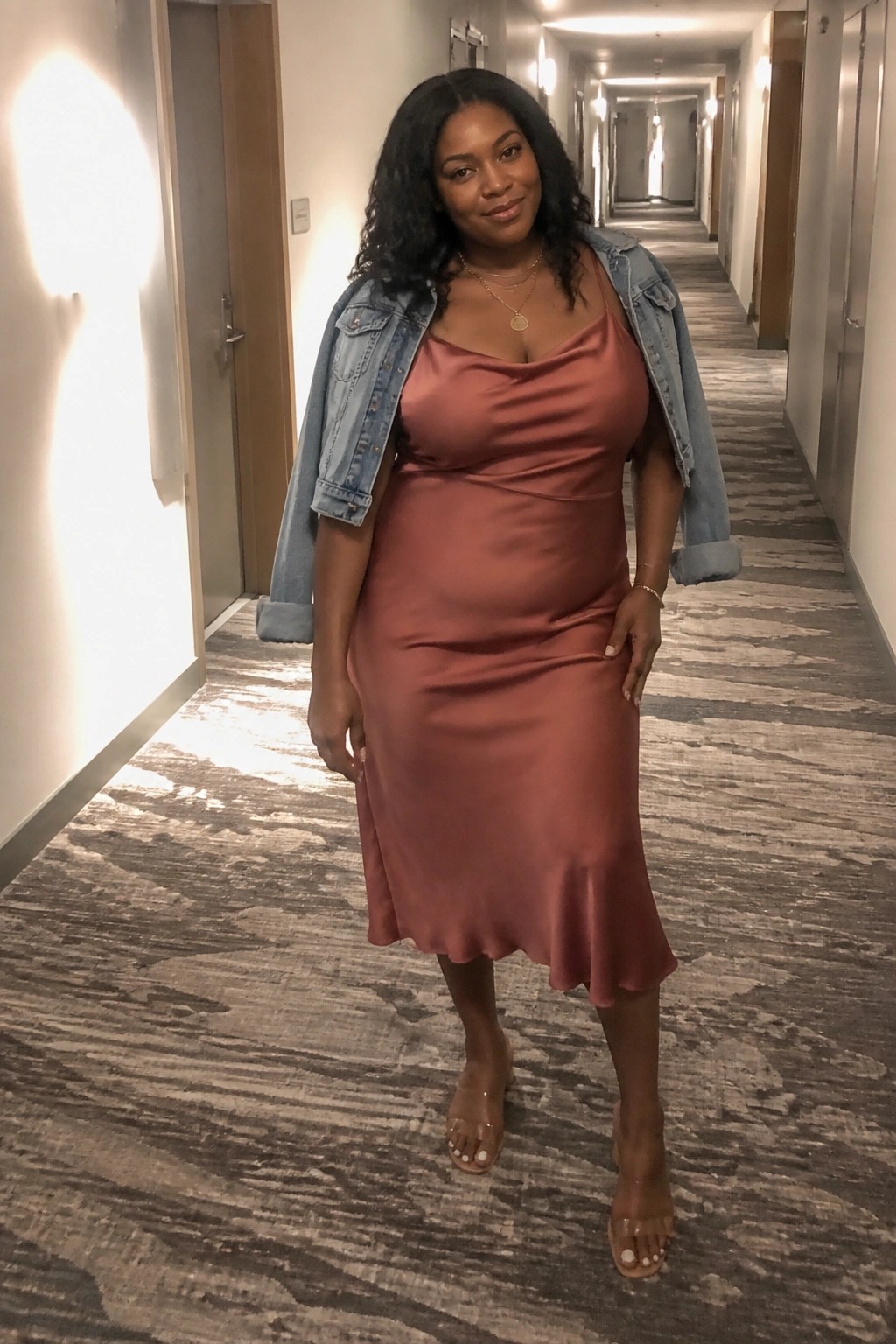 Woman in rose satin slip dress with denim jacket in hotel hallway